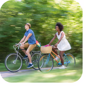 Two individuals cycling side by side on a scenic road, enjoying a sunny day outdoors.