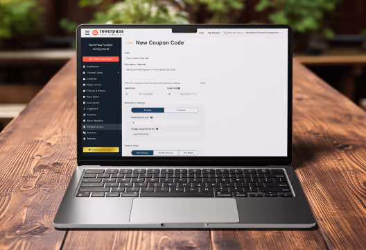 Laptop on a wooden table showing the RoverPass dashboard with the New Coupon Code form for creating promo codes