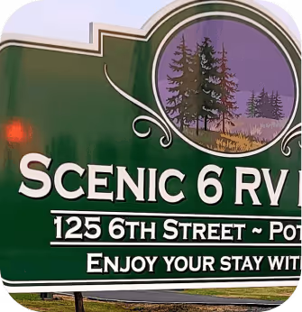 A welcoming sign at a scenic RV park, surrounded by lush greenery and inviting landscapes for travelers to enjoy.