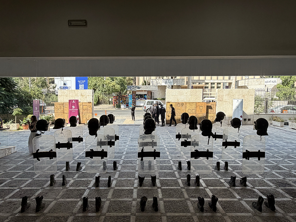 Anatomy of Fragility by Khaled Barakeh, rear view of the installation showing the backs of the riot shields and the empty spaces between helmets and boots.