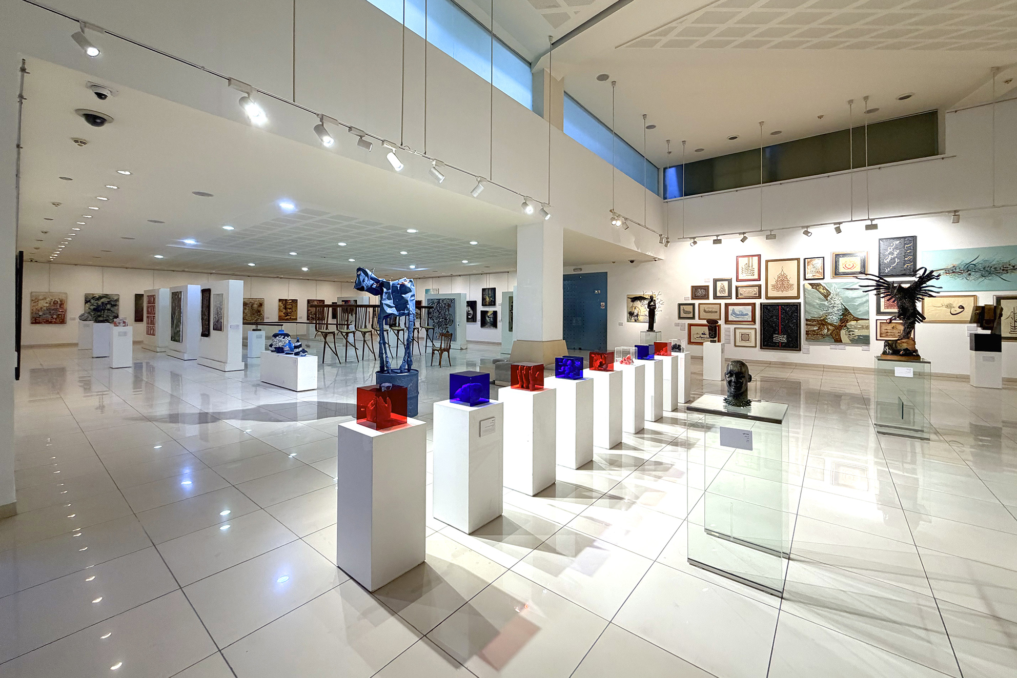 Sculptures in coloured display cases and paintings across the exhibition hall at Art Leaves Its Mark, 2026. Photograph by Khaled Barakeh.