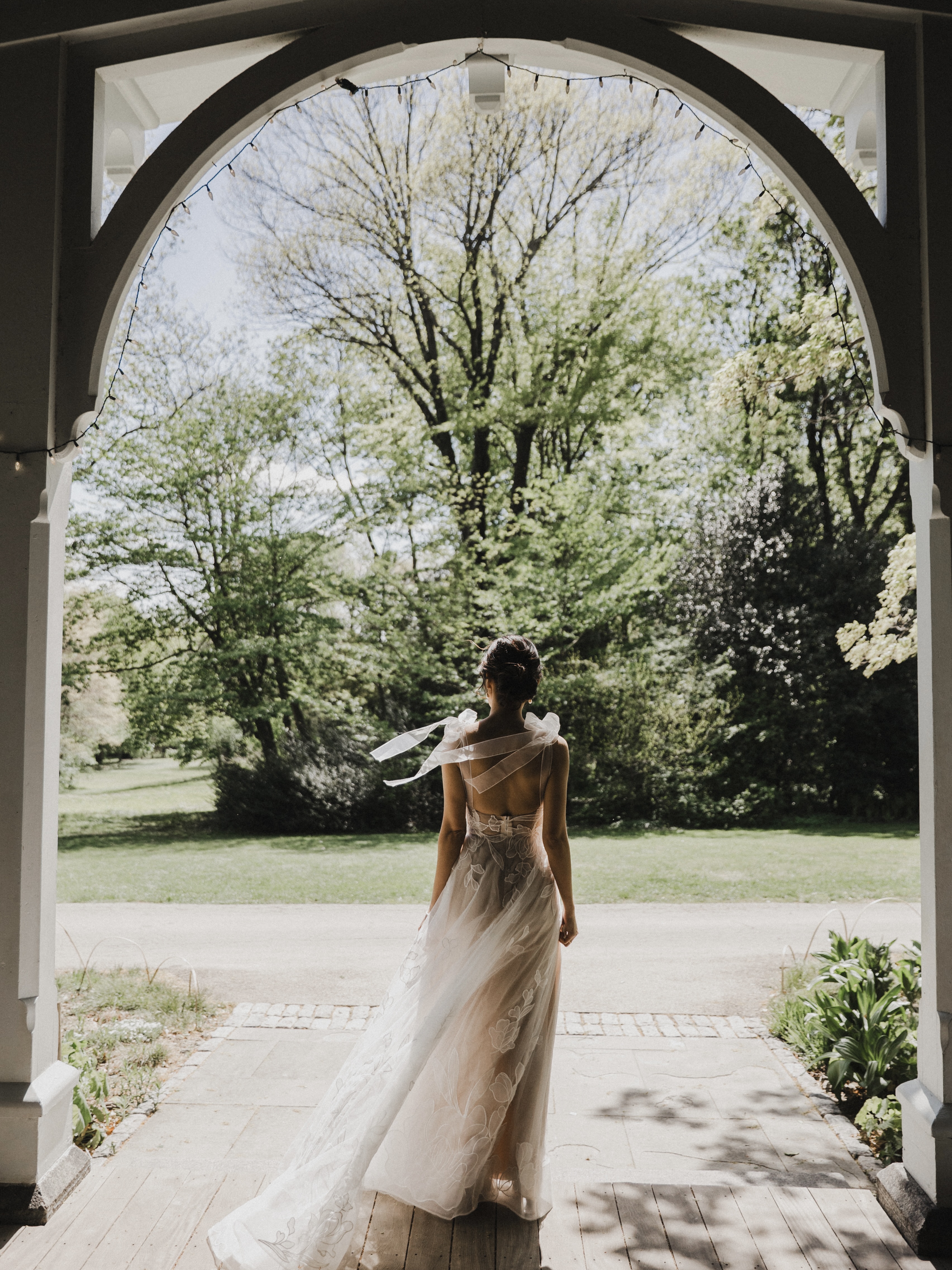 Bride looking out window onto the grounds of Portico Awbury Arboretum as guests arrive for the wedding