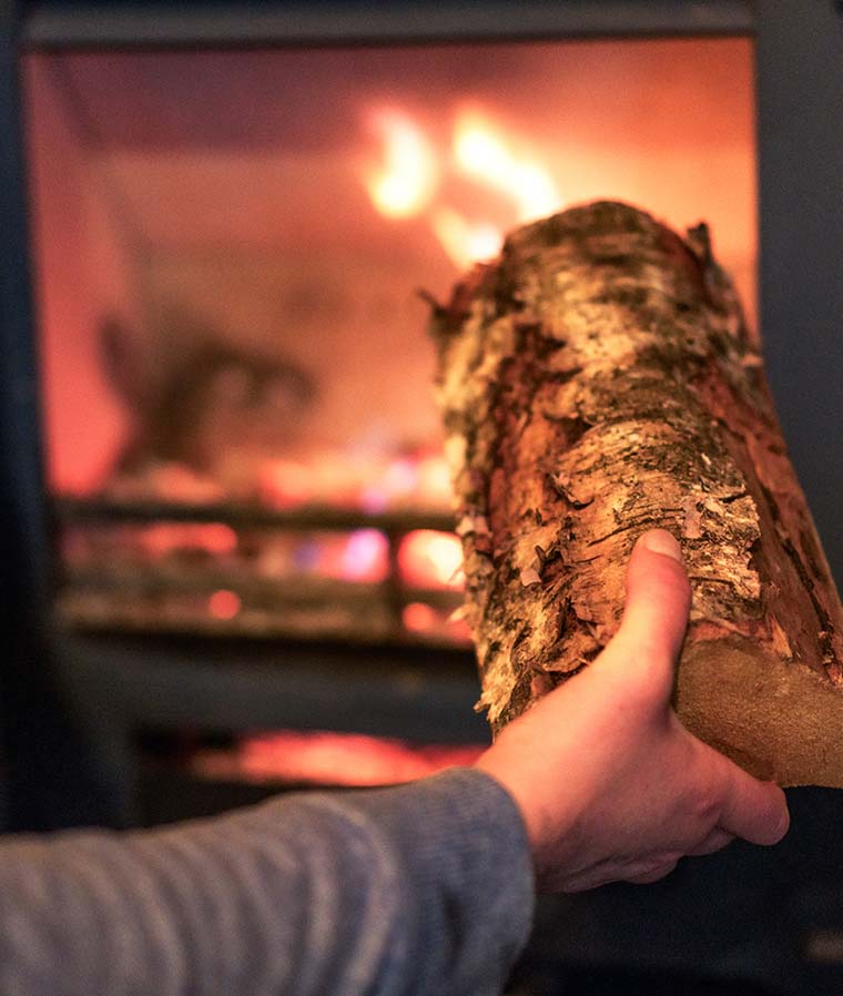 A closeup of someone putting a piece of wood into a lit wood stove.