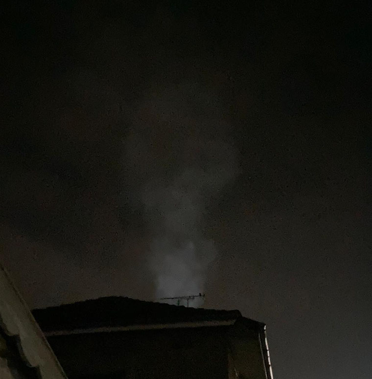 Smoke rises from a chimney at night.