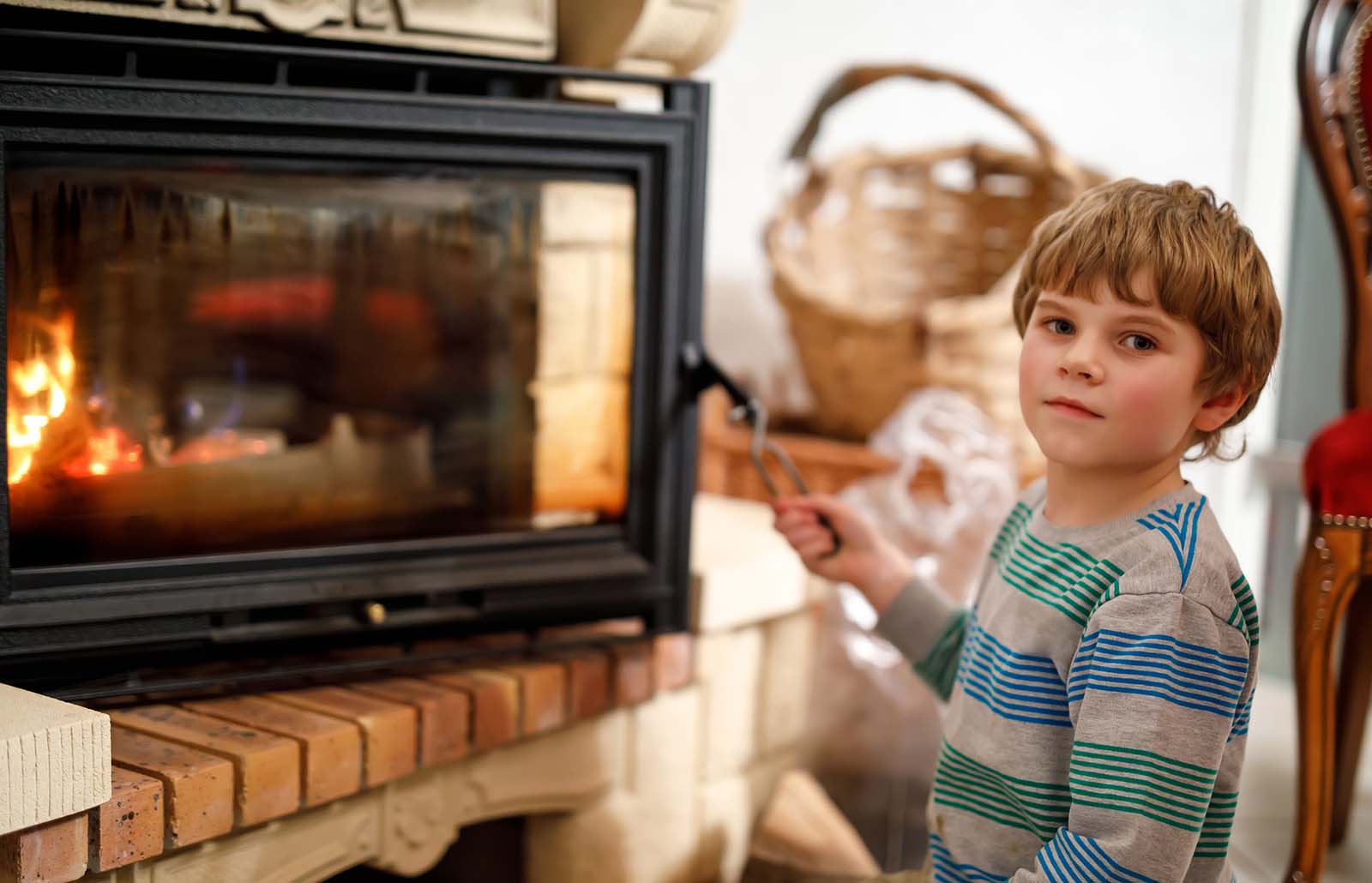 A boy sits in front of a lit wood stove with the door open.