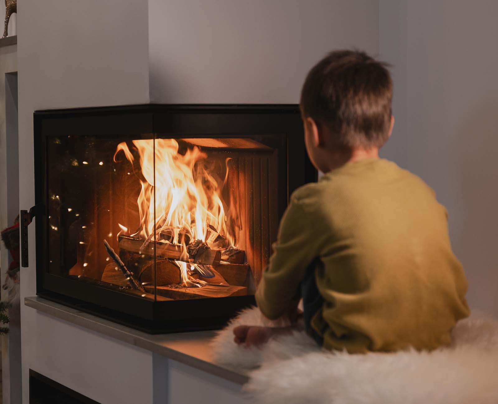A boy sits looking at a fire burning in a modern wood burner.