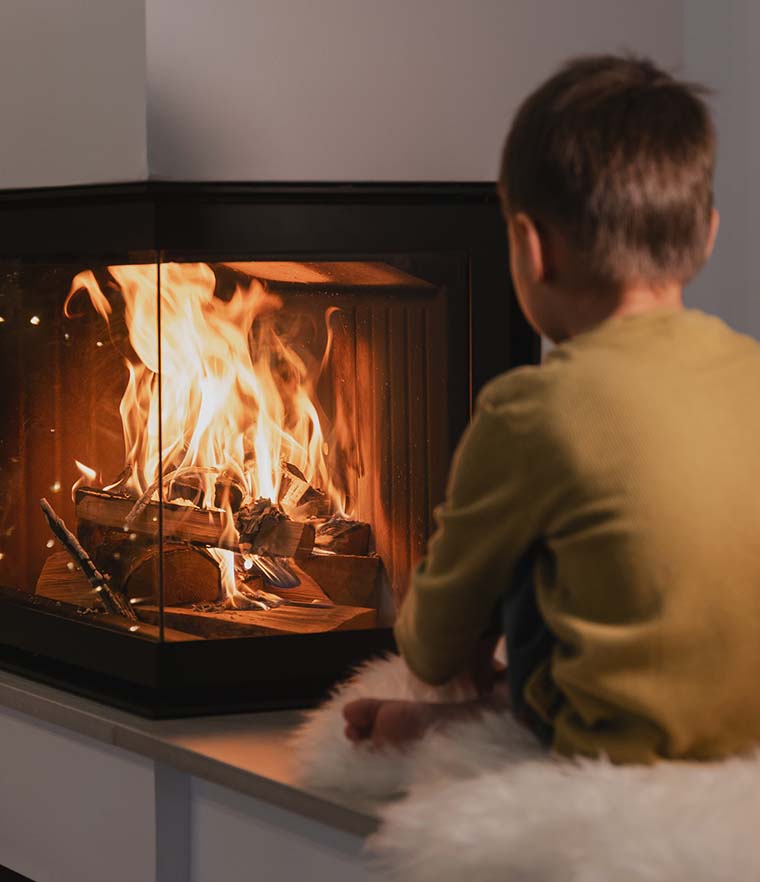 A boy sits looking at a fire burning in a modern wood burner.
