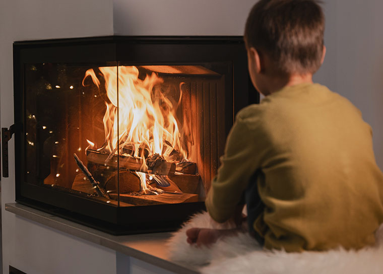 A boy sits looking at a fire burning in a modern wood burner.