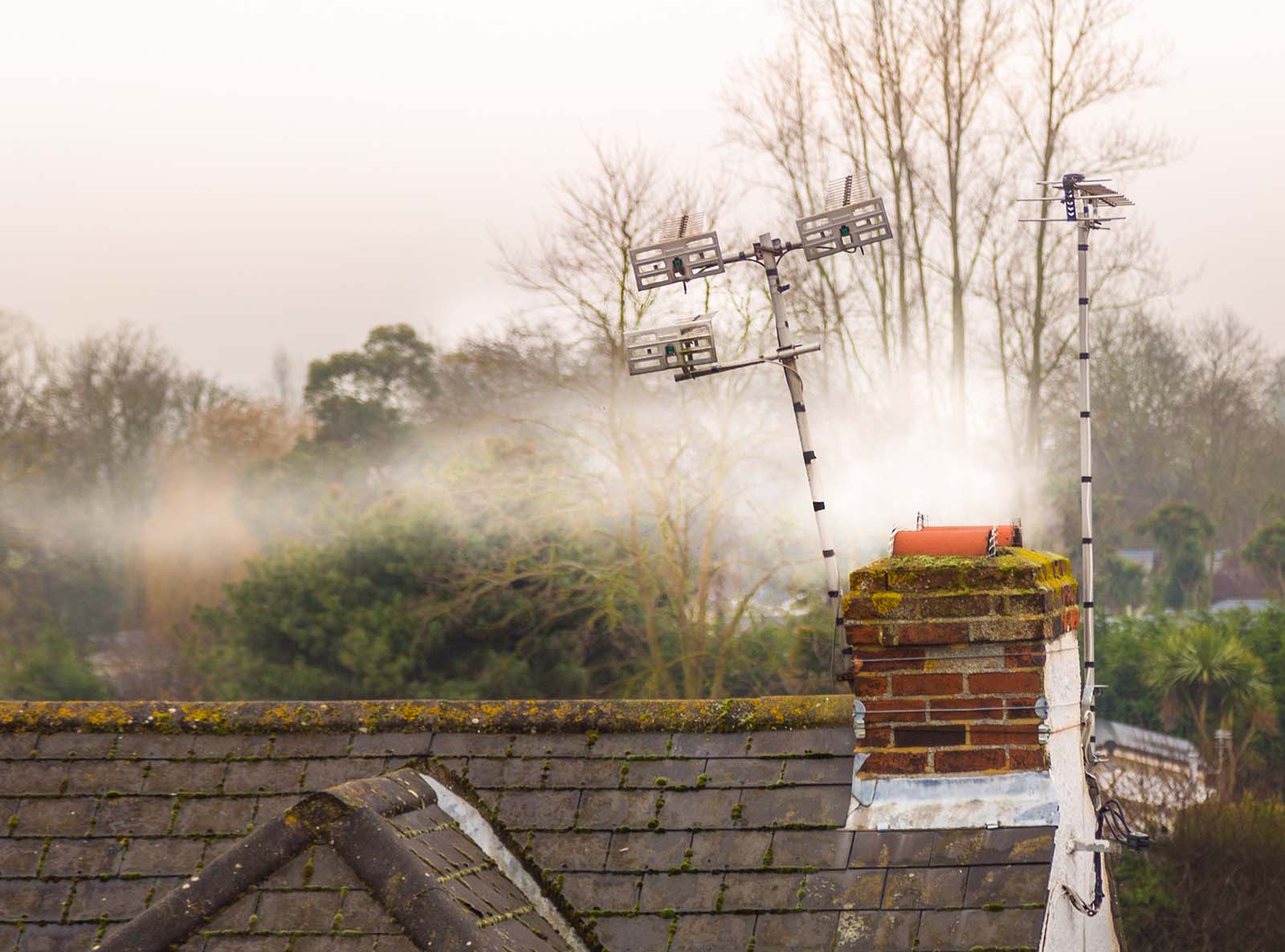 Smoke rises from a chimney next to a television antenna. 