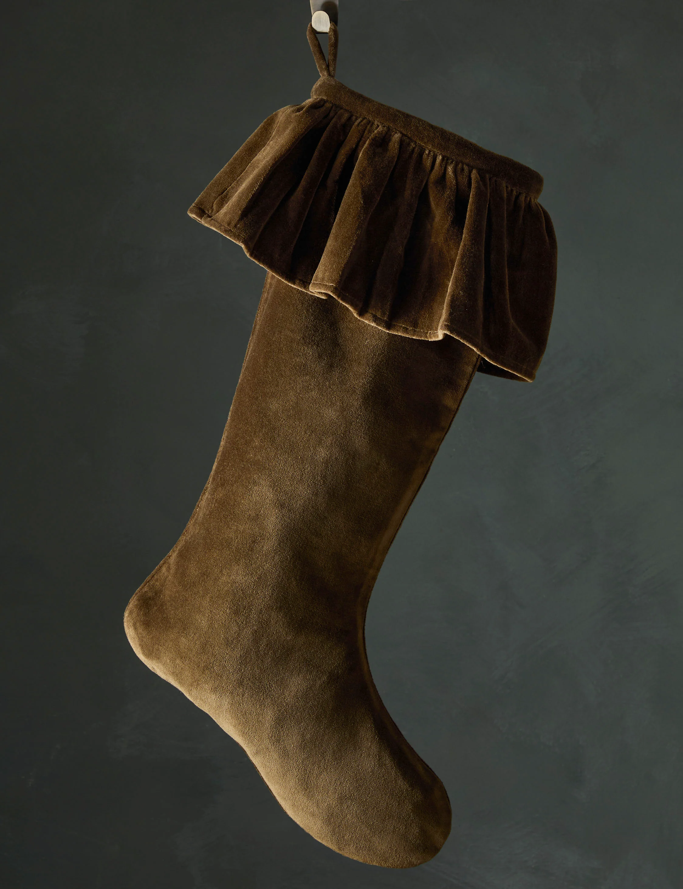 Olive green velvet Christmas stocking with a ruffled cuff hanging against a dark background.