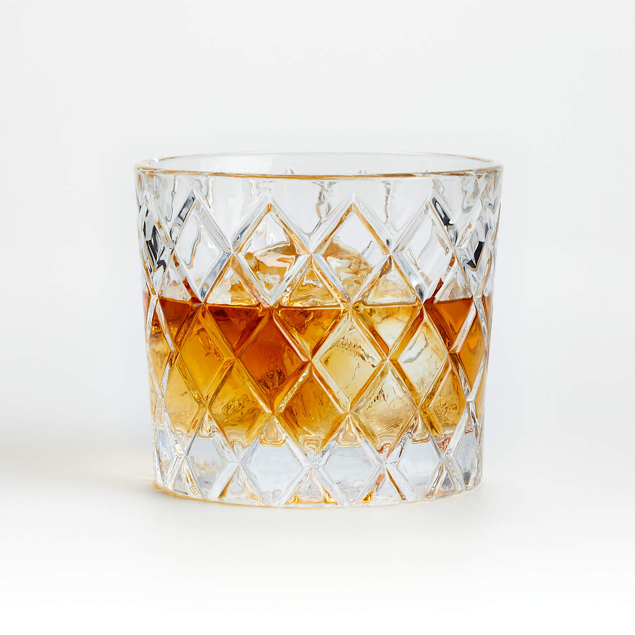 Cut crystal glass with amber liquid and ice cubes on a white background.