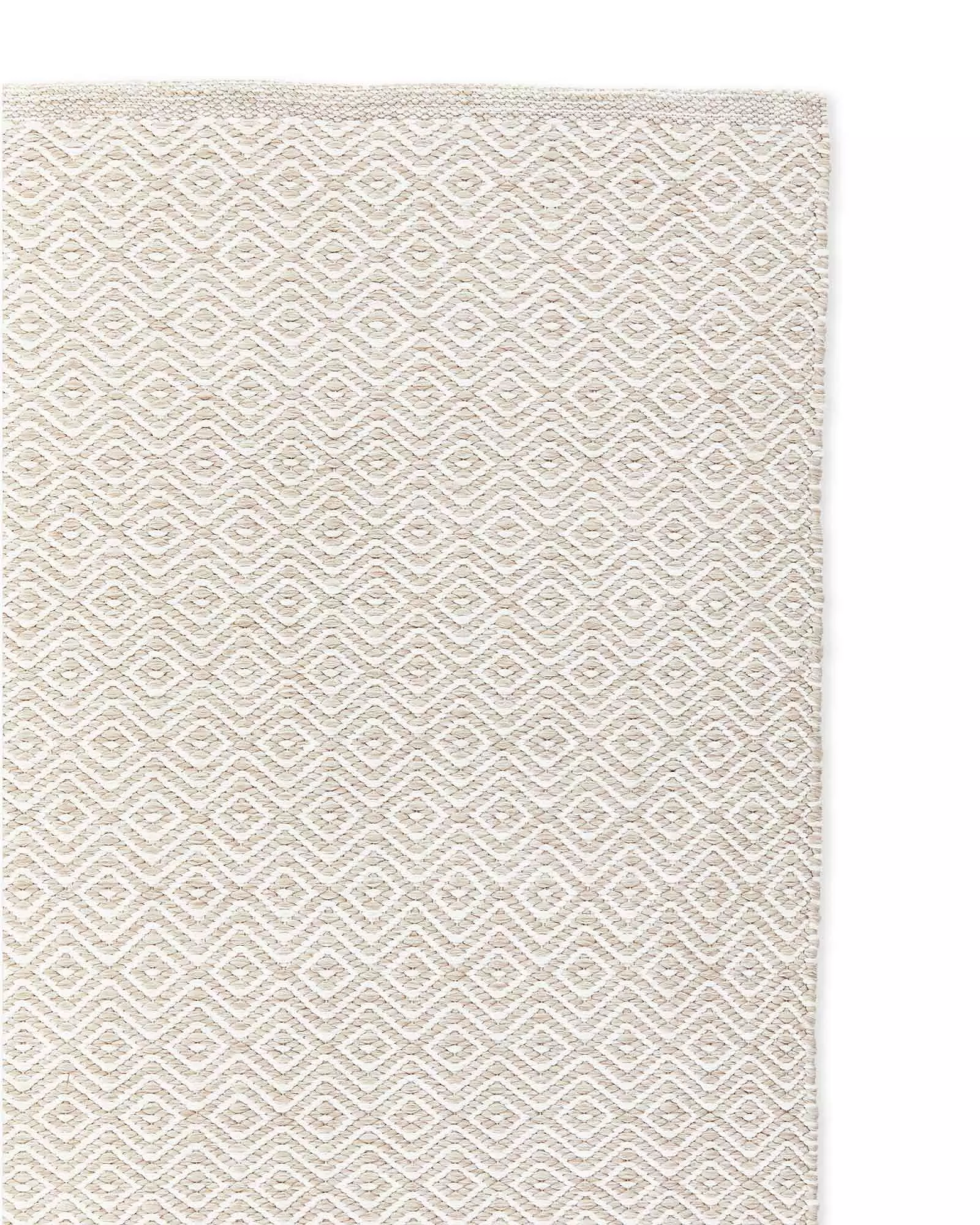 Close-up of a woven beige and off-white rug with a diamond pattern.