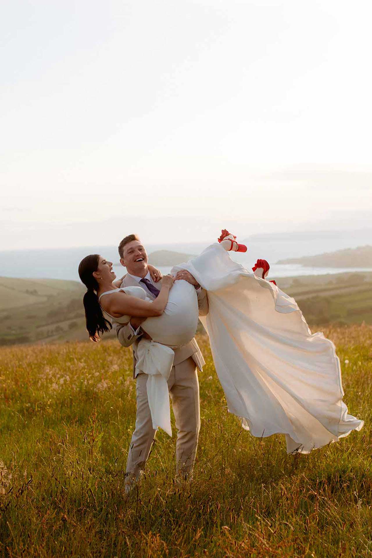 Groom sweeps bride off her feet on the hills at devonshire coast wedding, captured by Cheshire Wedding Photographers Paul and Nanda.