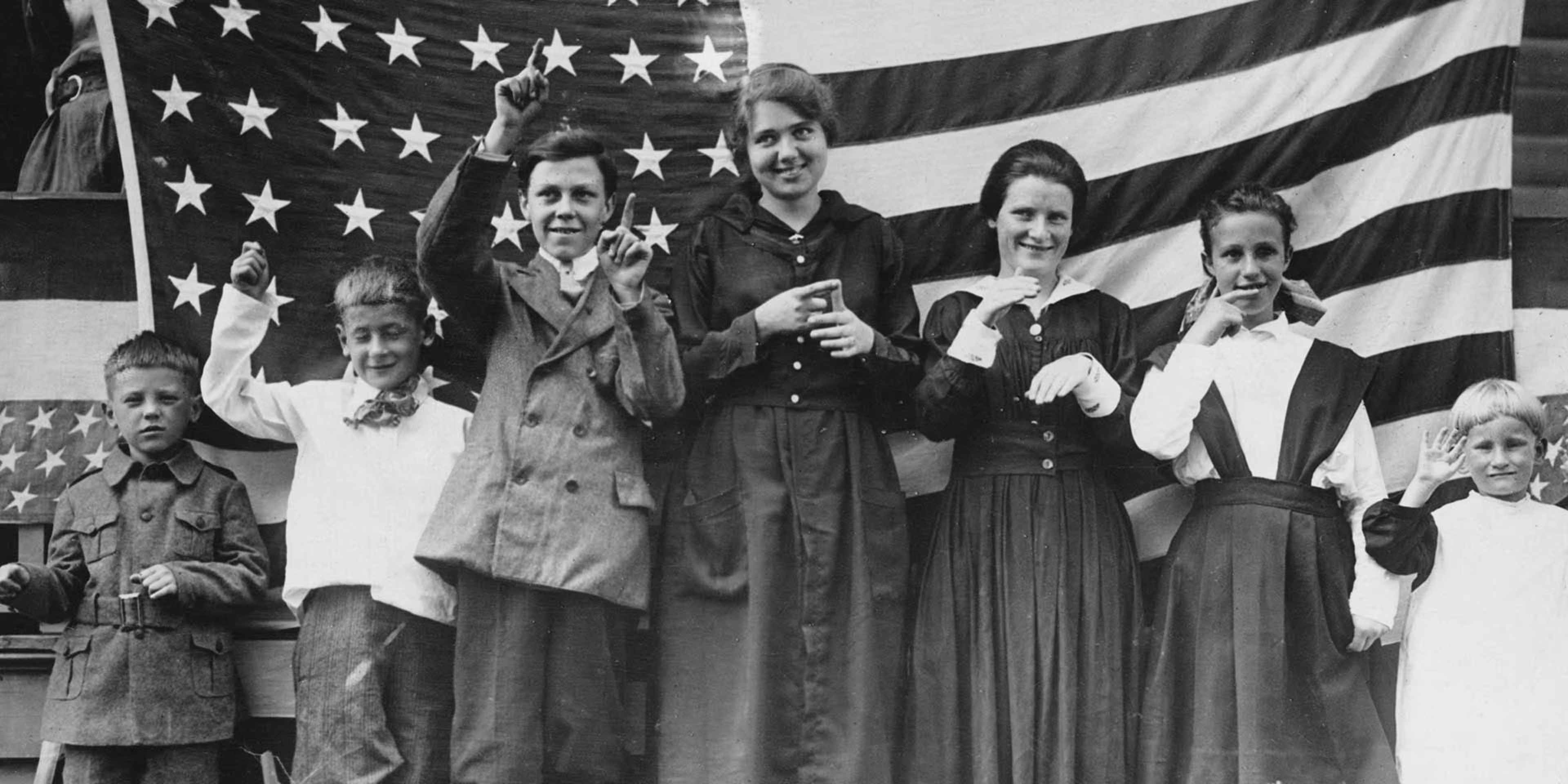 deaf students in front of an american flag doing signs and smiling