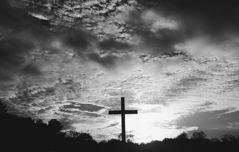 a black and white image of a cross against a cloudy sky