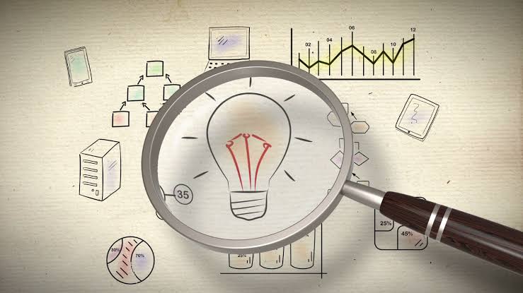 Magnifying glass focusing on a hand-drawn light bulb illustration surrounded by various business-related sketches including charts, graphs, a flowchart, a server, and electronic devices on a textured background.