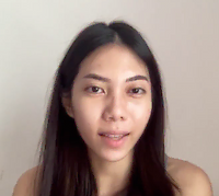 Young woman with long dark hair and light makeup looking at the camera against a plain light background.