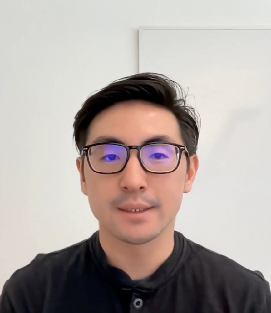 Man with short black hair and glasses wearing a dark shirt, facing forward against a plain light background.
