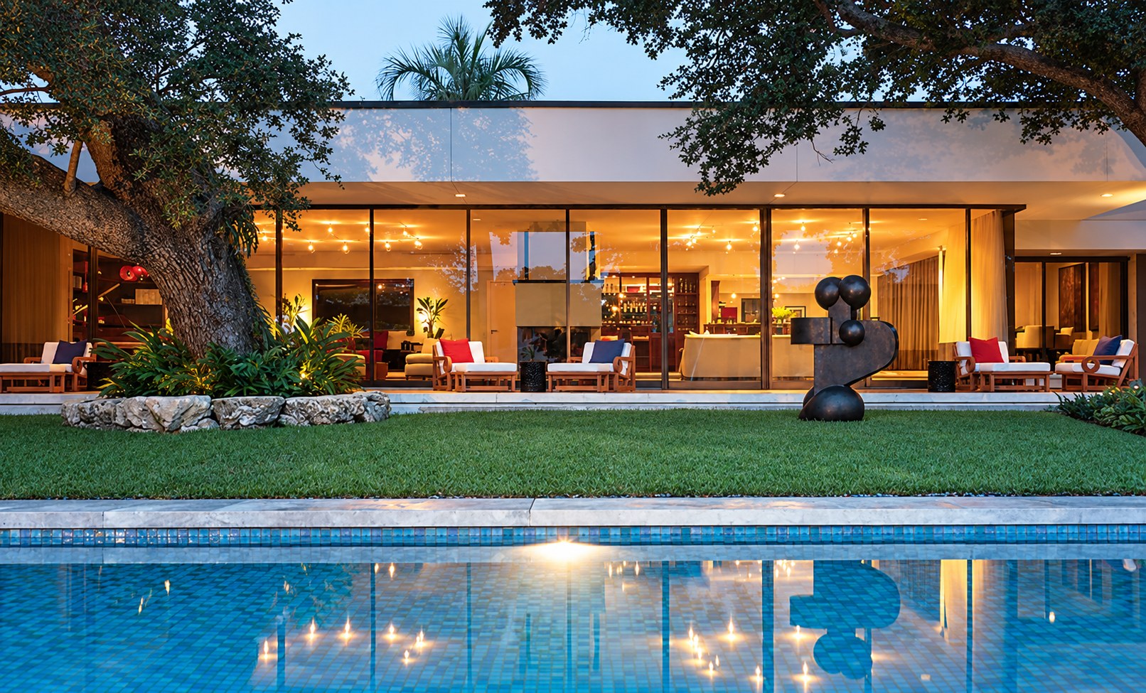 Glass house lit at dusk behind a long pool
