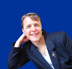 Photo of Kerryn. She has short light hair and is wearing a navy suit jacket and white shirt against a blue background.