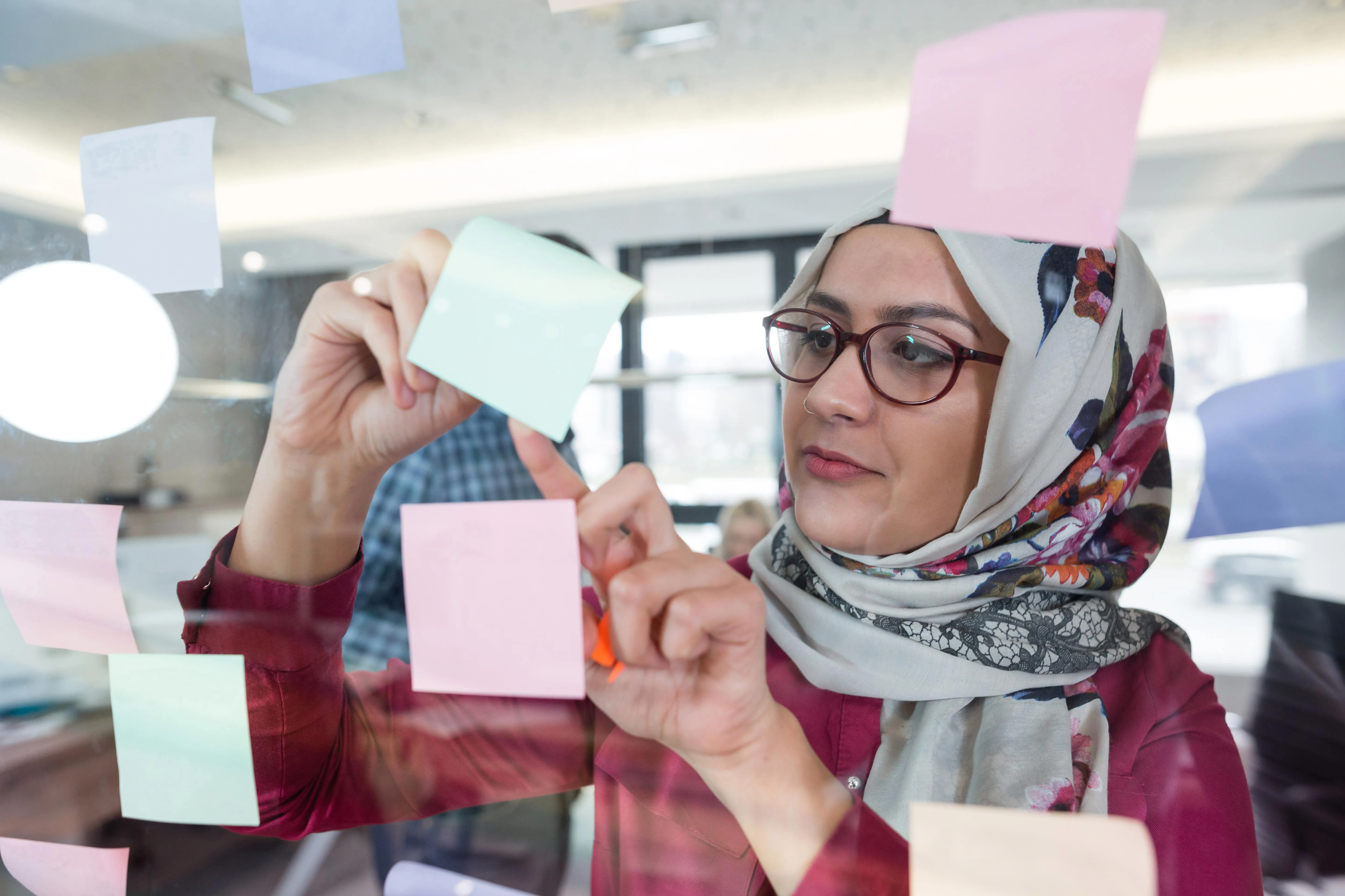 An image of a lady writing on sticky notes on a glass window.