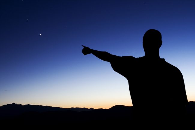 Photo taken at sunset, showing the silhouette of a man pointing at the North Star