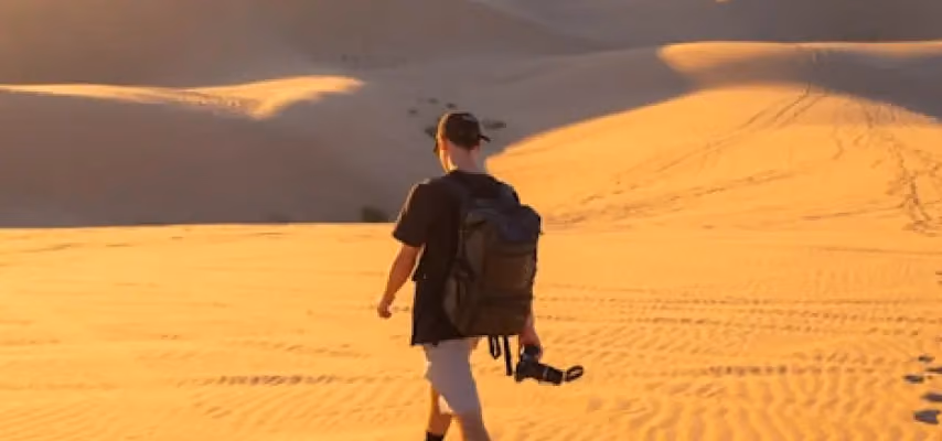 Uomo che cammina nel deserto con zaino e macchina fotografica