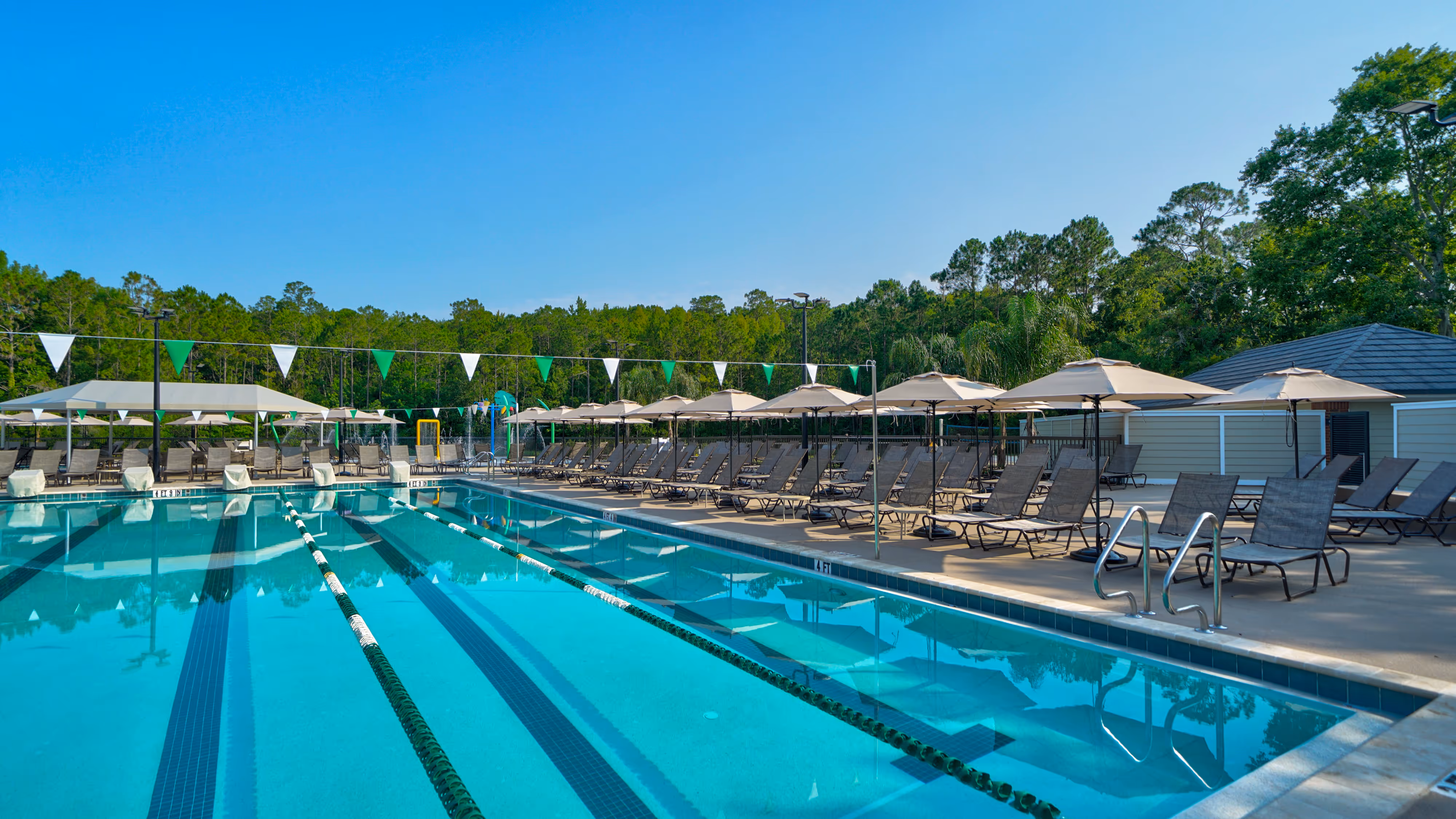 Outdoor swimming pool with lane dividers, surrounded by lounge chairs and umbrellas on a sunny day.