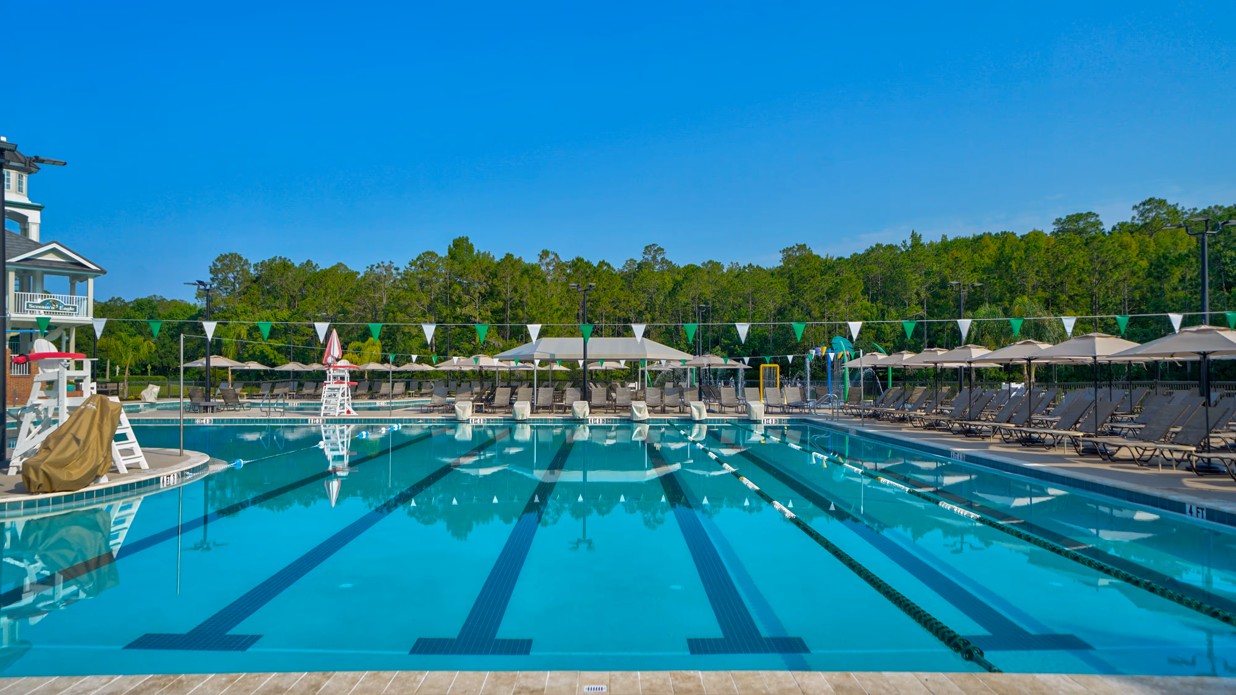 Outdoor swimming pool with lanes, surrounded by lounge chairs and umbrellas under clear blue sky.