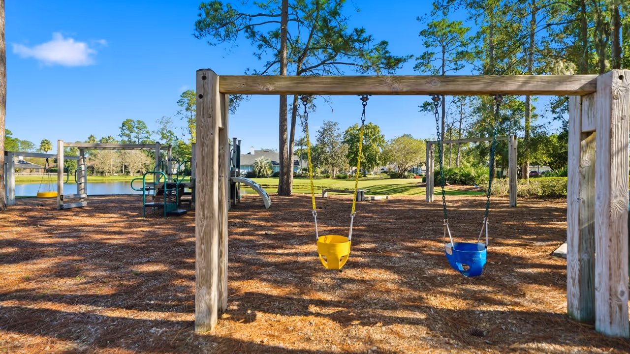 Playground with yellow and blue toddler swings, slide, and other play structures under a clear blue sky.