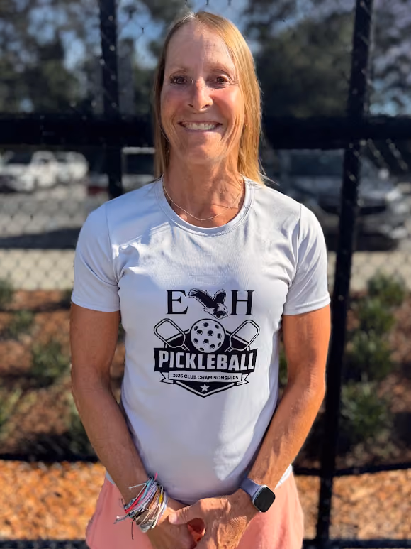 Smiling woman wearing a white Pickleball 2025 Club Championships shirt and multiple bracelets outdoors.