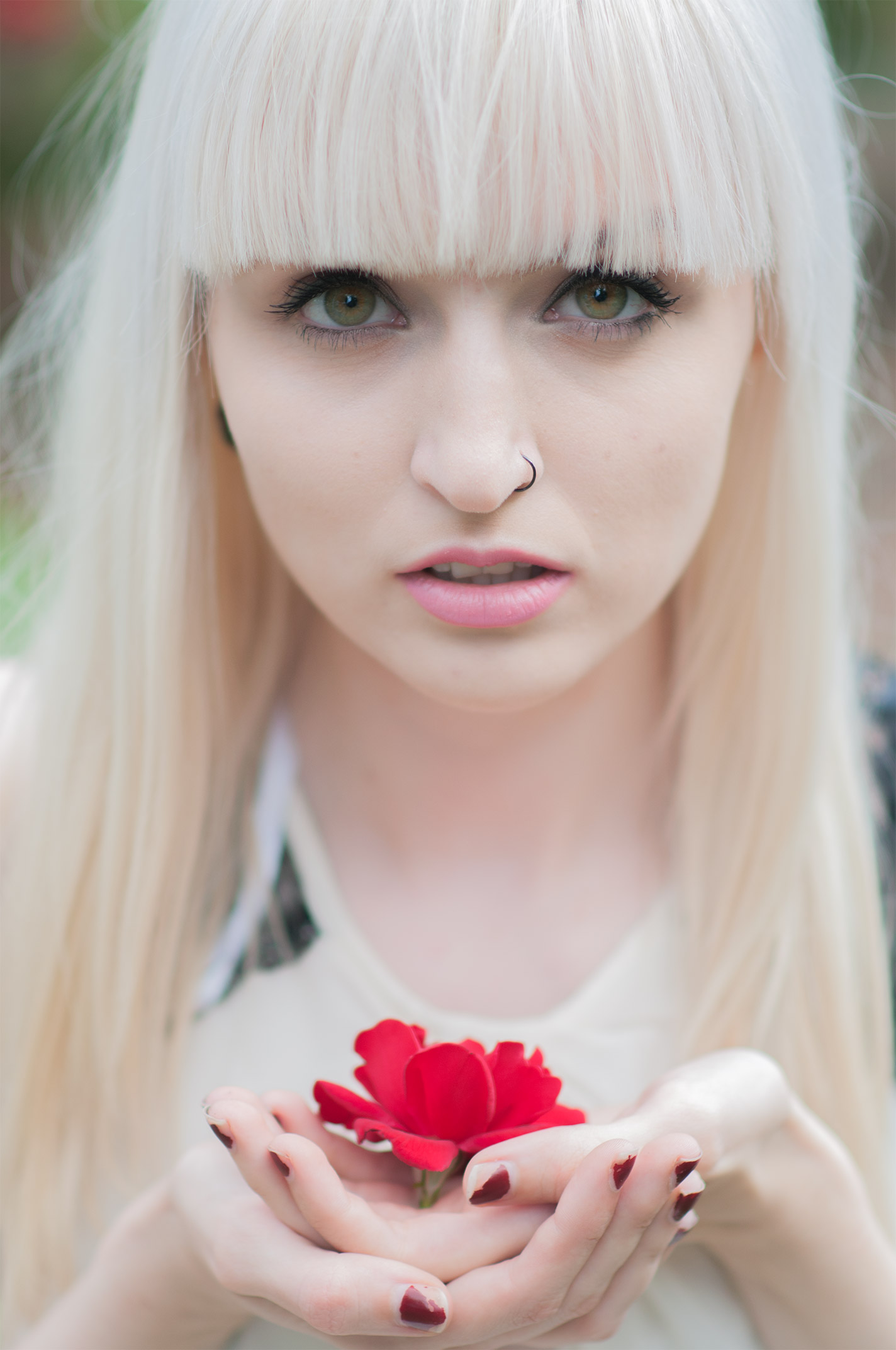 Original portrait of a pale woman with a platinum fringe holding a red flower, before retouching