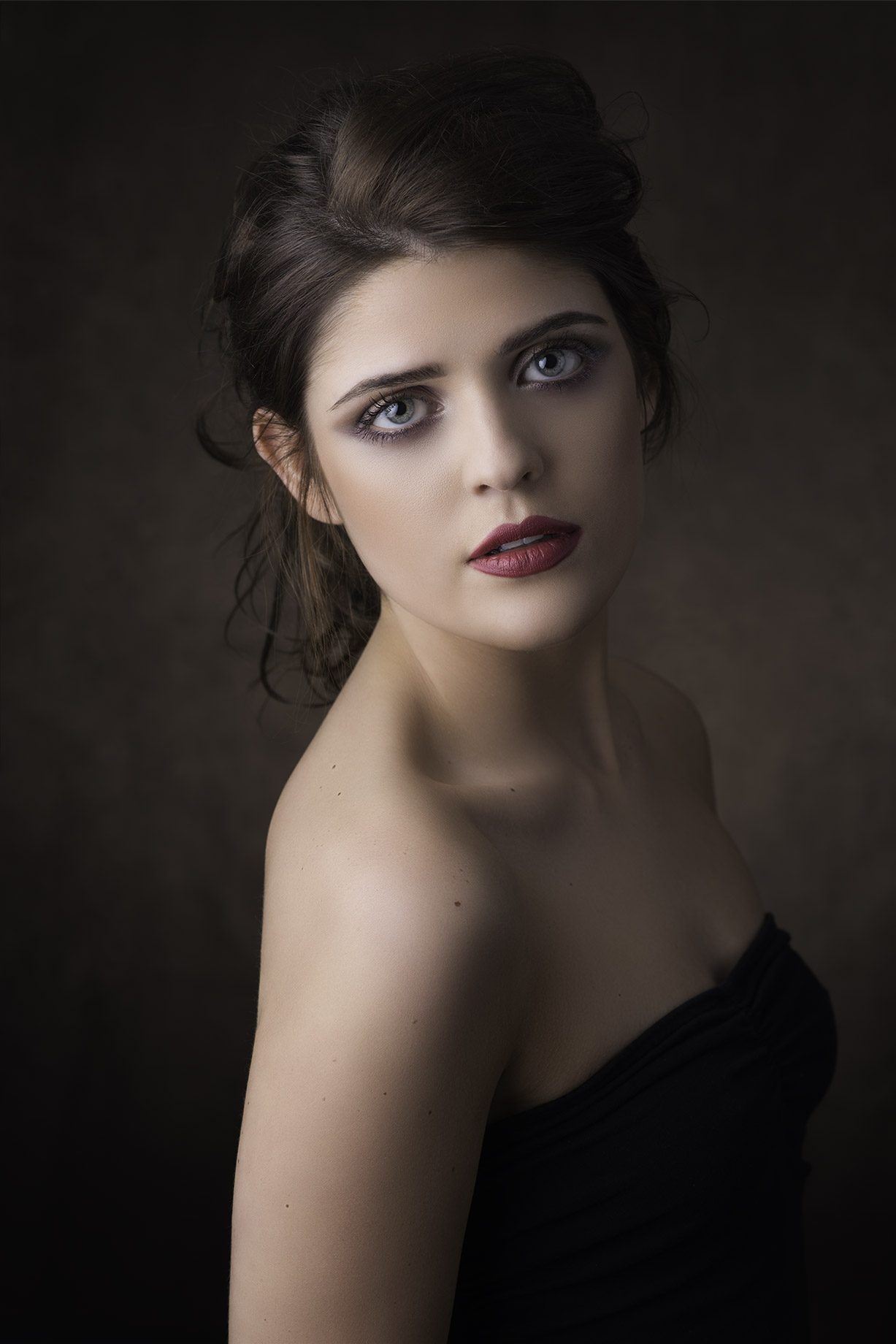 Retouched portrait of a dark-haired woman in a strapless black top against a dark background (after)
