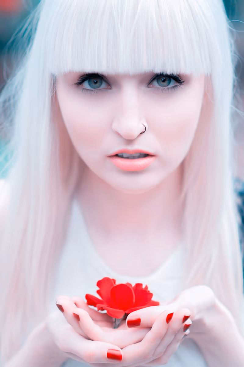Retouched portrait of a pale woman with a platinum fringe holding a red flower in cupped hands (after)