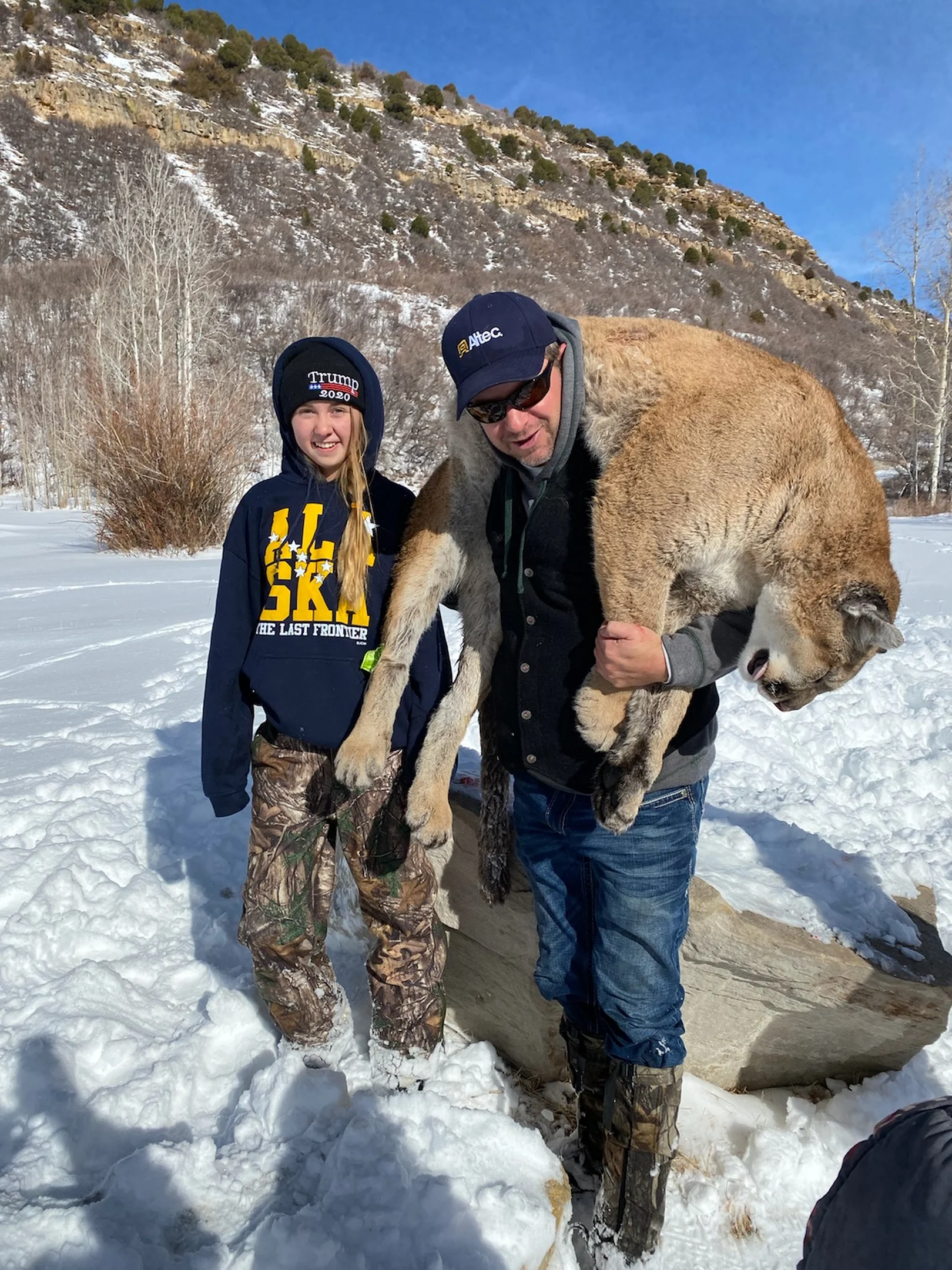 Man carrying a mountain lion over his shoulders standing next to a smiling girl in snowy landscape.