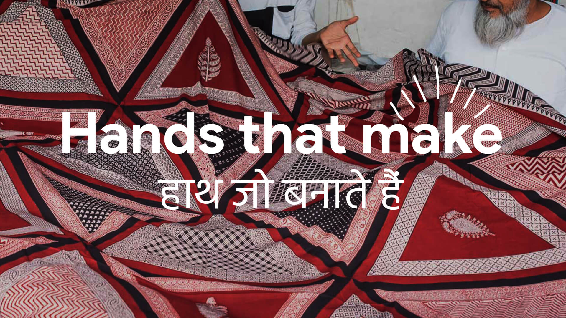 Two men holding a large red and black patterned textile with the text 'Hands that make' and Hindi script overlay.