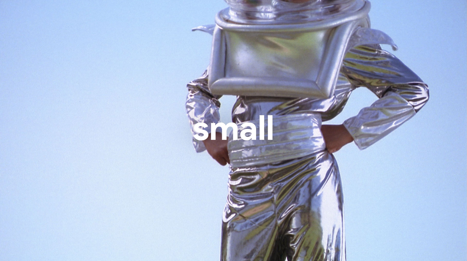 Person wearing a shiny silver space suit with hands on hips against a clear blue sky.