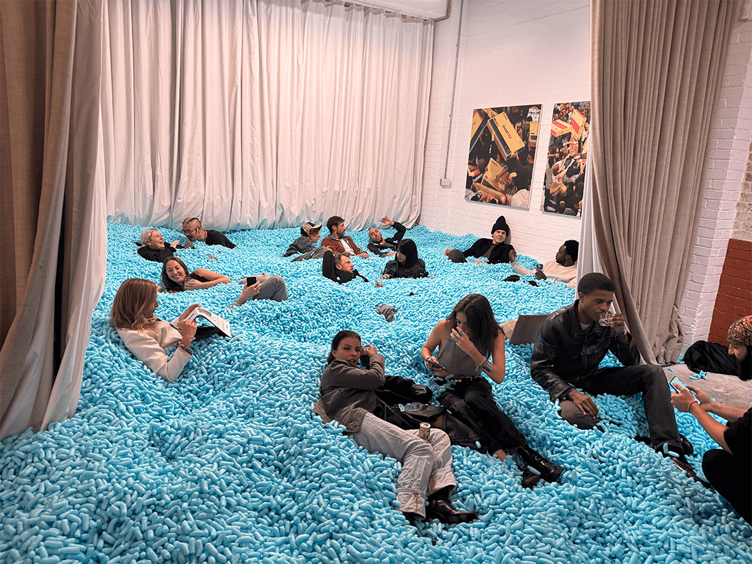 A group of people lounging and interacting while sitting and lying in a large indoor pool filled with blue packing peanuts.