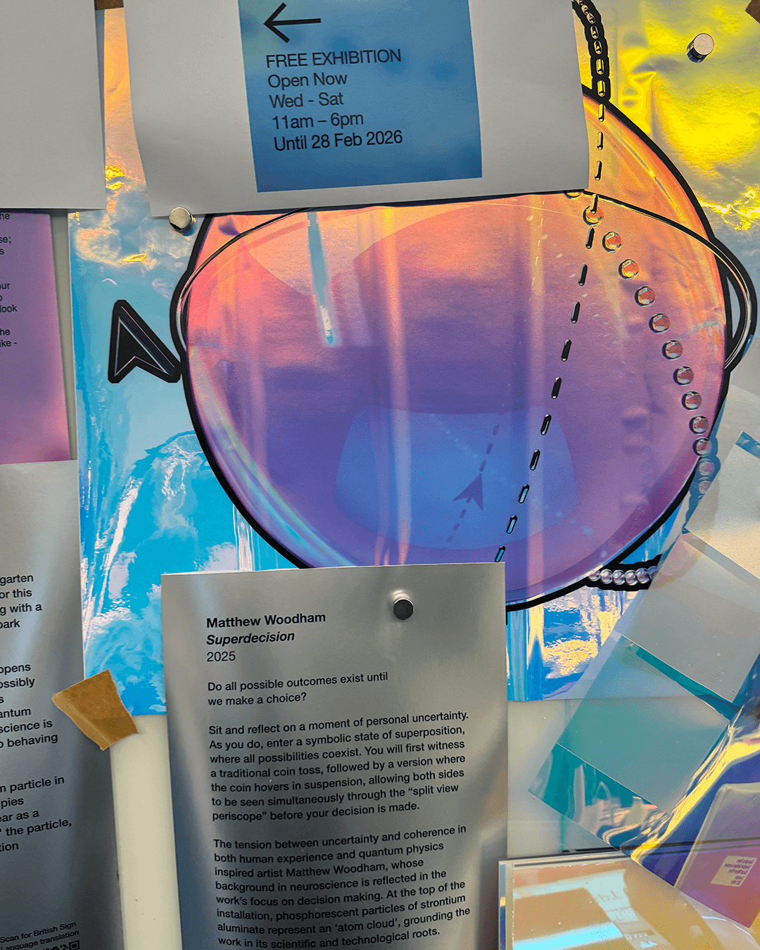 Exhibition details and description of Matthew Woodham's 2025 artwork 'Superdecision' displayed on a colorful reflective background with pinned papers.