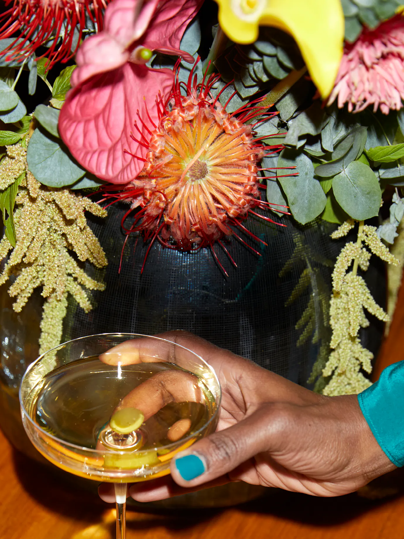 Cocktailglas vor großem, farbenfrohem Blumenarrangement