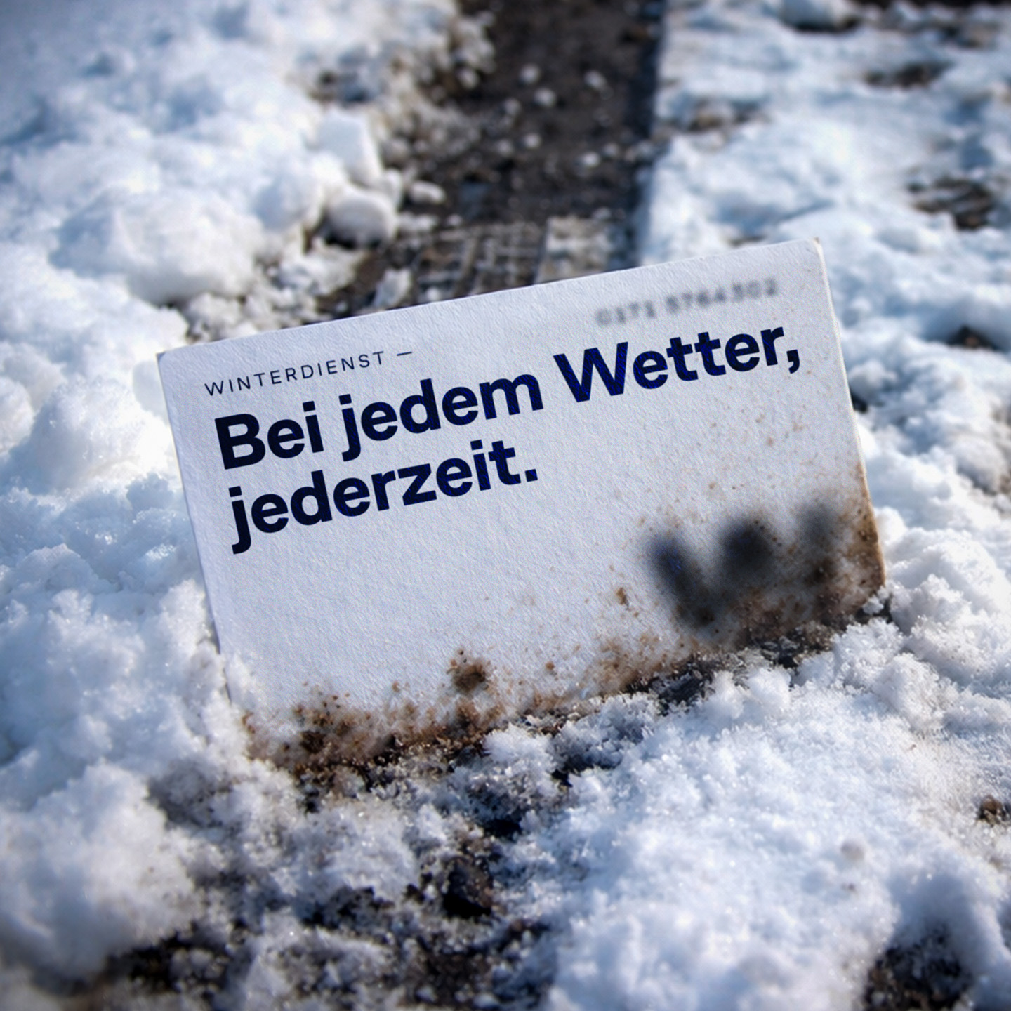 business card with winter emergency call services of a facility management business, stuck into dirty snow in a messy driveway. Designed by Lisa Gawenda