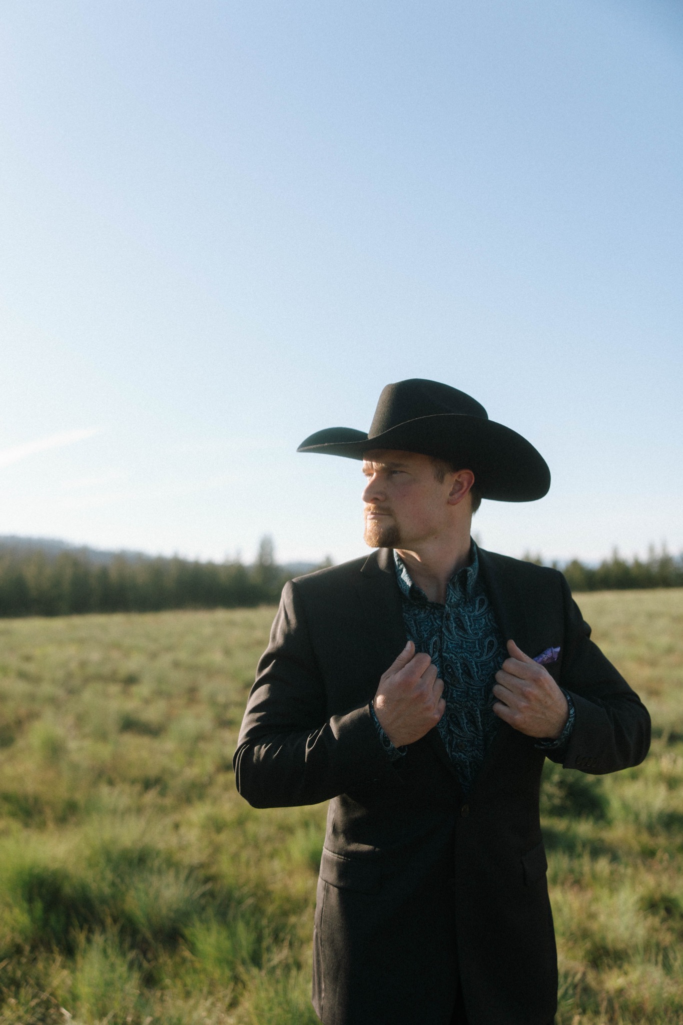 RMF DJ Josh Backer wearing a cowboy hat and suit in a Montana field