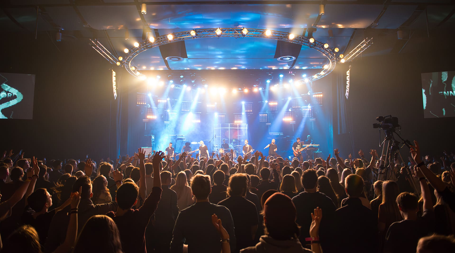 Publikum vendt mot en sterkt opplyst scene med et band som fremfører livemusikk på et konsertsted.