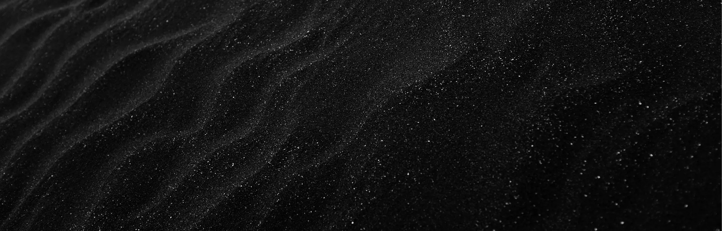 Close-up of textured black sand with subtle wave-like patterns and small sparkling grains.