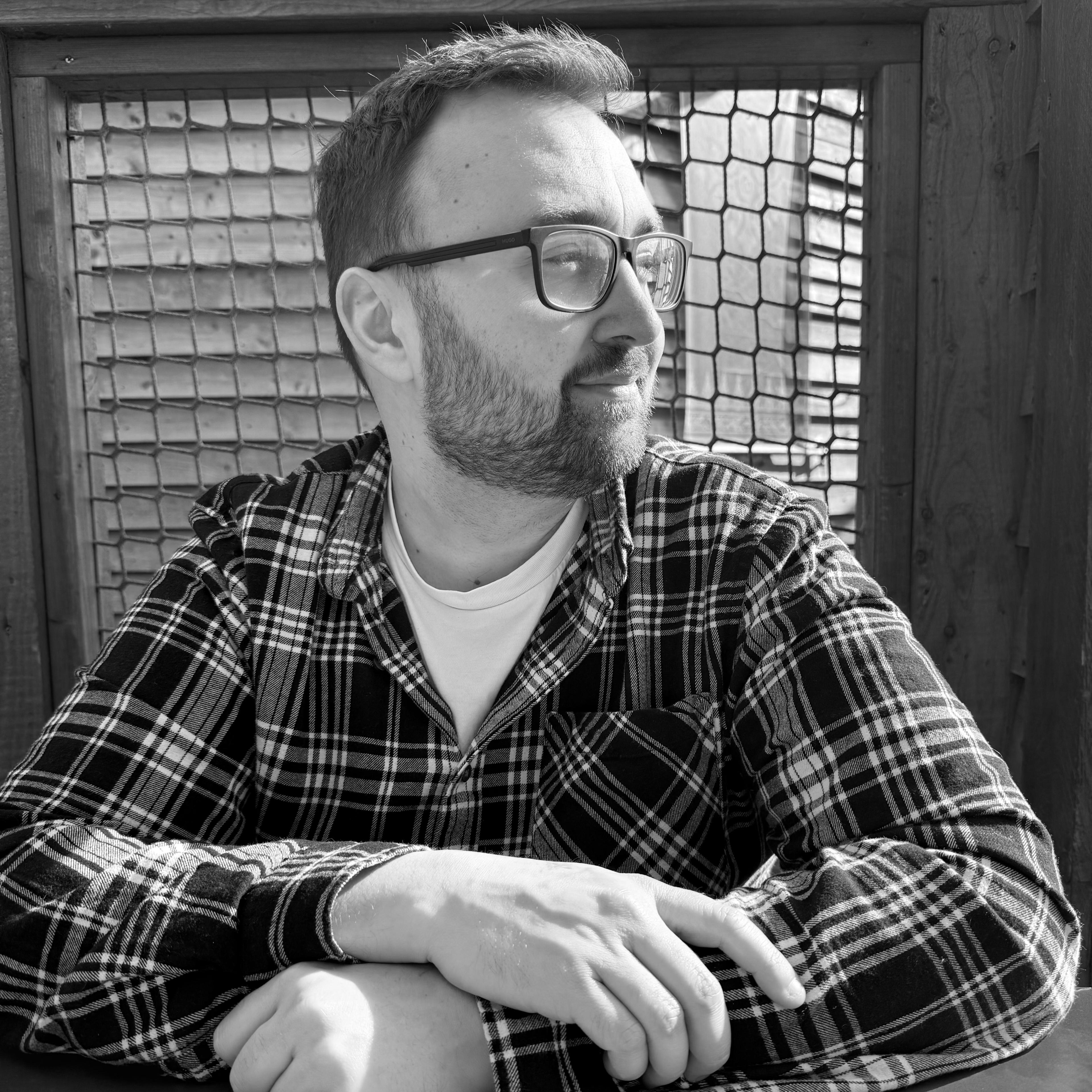 Smiling man with glasses and a beard wearing a navy blue t-shirt against a plain grey background.