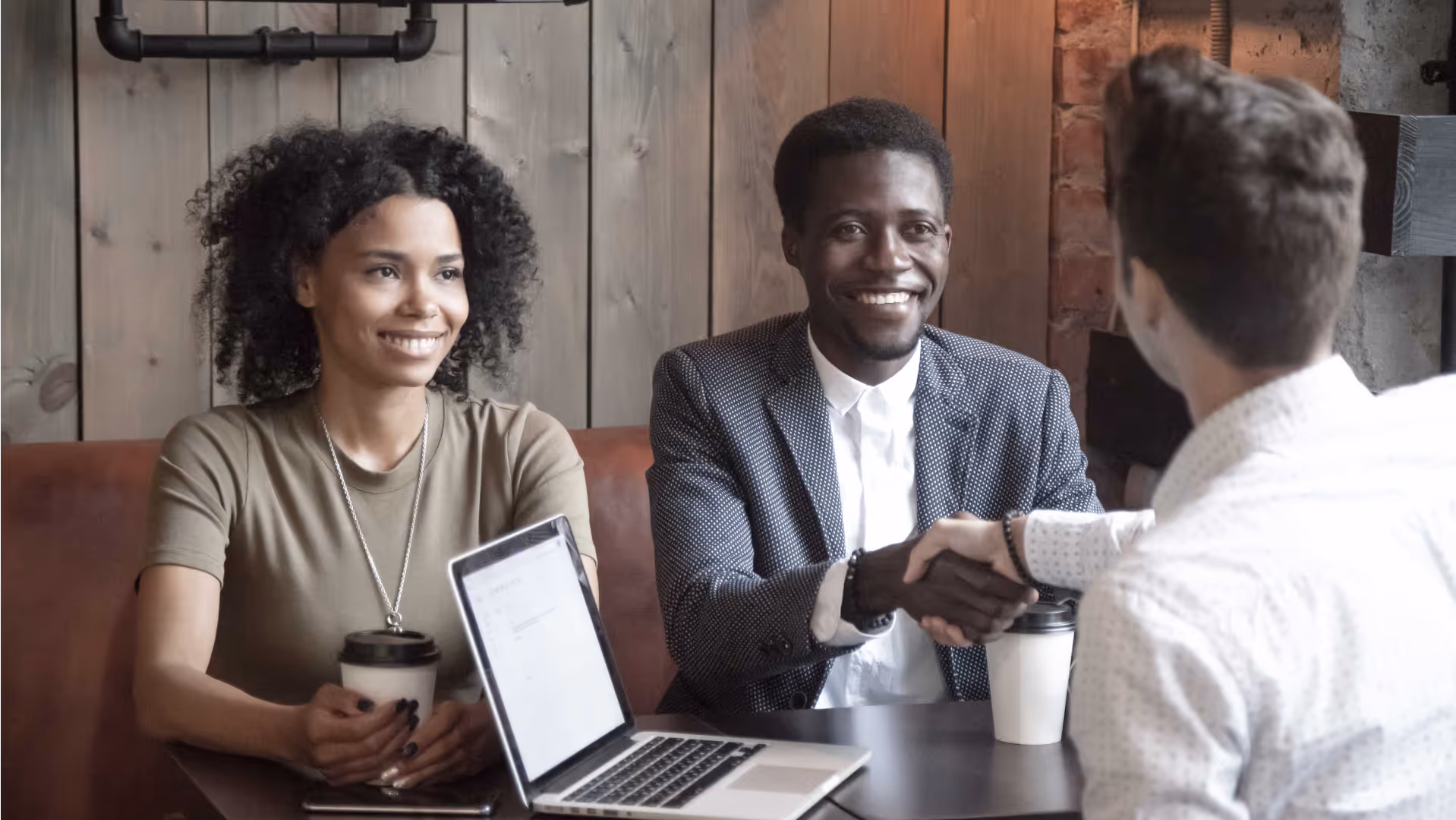 People smiling at a business meeting, with one shaking hands across the table.
