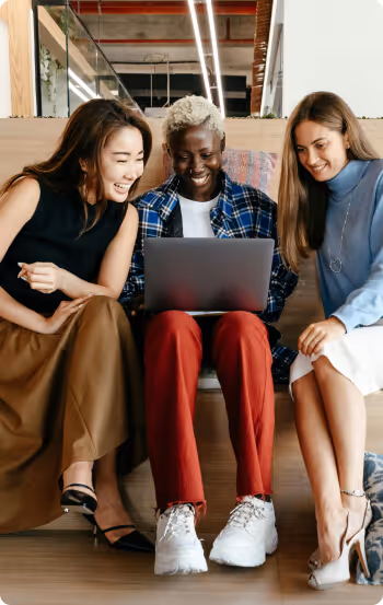 Three colleagues sitting together, smiling, and collaborating on a laptop using Formstack in a modern office setting.