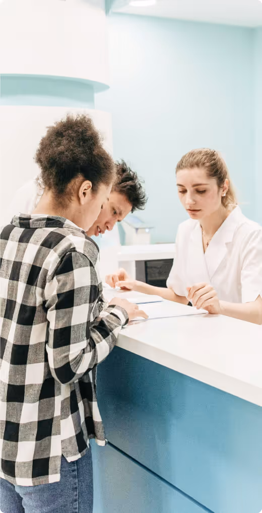 Two people stand at a reception desk speaking with a staff member utilizing Formstack for a healthcare check-in process.