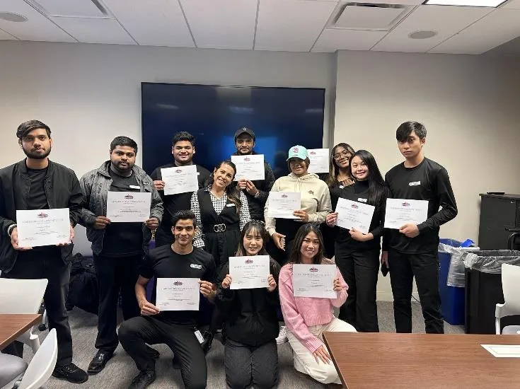 Group of people in a room holding certificates, smiling at the camera in a celebratory setting.