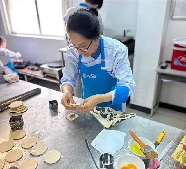 Woman in blue apron shaping dough with filling in a kitchen with cooking tools on the table.